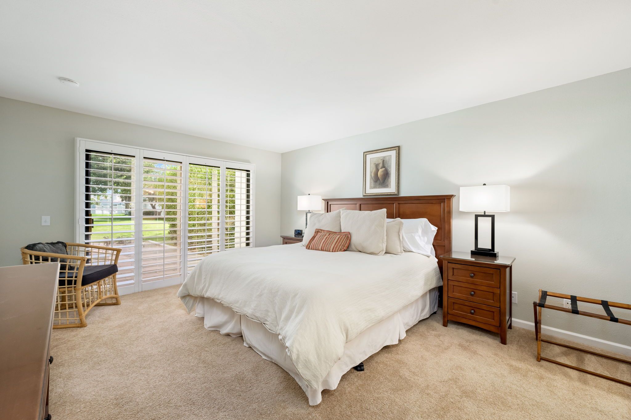 A bedroom with a large bed, a nightstand, a chair, and a wooden bench.