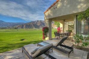 A patio with two lounge chairs, a table, and chairs, overlooking a green field and mountains. - Santa Rosa Cove #50, 3 Bedrooms   3.5 Baths  La Quinta City Permit 063498 (La Quinta)