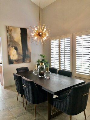 Un comedor moderno con una mesa rectangular, sillas oscuras, una lámpara de araña original y un cuadro abstracto grande en la pared.