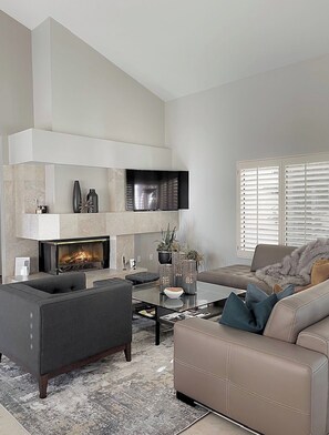 A modern living room with a fireplace, a flat-screen TV mounted on the wall, and a comfortable seating area with a sofa and armchairs. - Santa Rosa Cove #57, 3 bedroom/2bath, Permit 063491 (La Quinta)