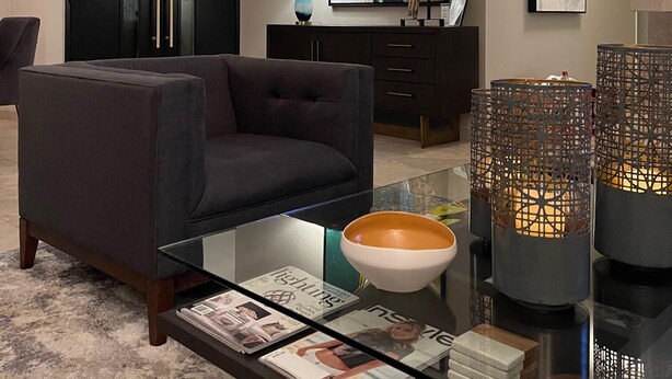 Ein modernes Wohnzimmer mit einem dunklen Sofa, einem Glastisch, Zeitschriften, Dekoration und abstrakten Bildern an den Wänden.