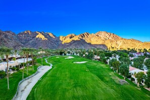 A golf course with a clear path, surrounded by trees and buildings, with mountains in the background. - Beautiful Home on Golf Course with Amazing Mtn Views! Permit 063495 (La Quinta)
