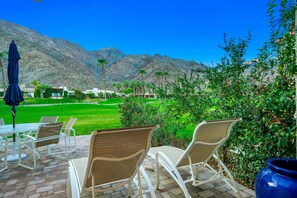 An outdoor patio with wicker chairs and a table, overlooking a well-maintained lawn and mountains. - Beautiful Home on Golf Course with Amazing Mtn Views! Permit 063495 (La Quinta)