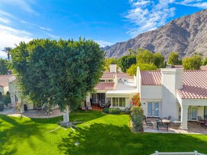 A residential area with houses featuring red-tiled roofs, a well-maintained lawn, and a mountain backdrop.