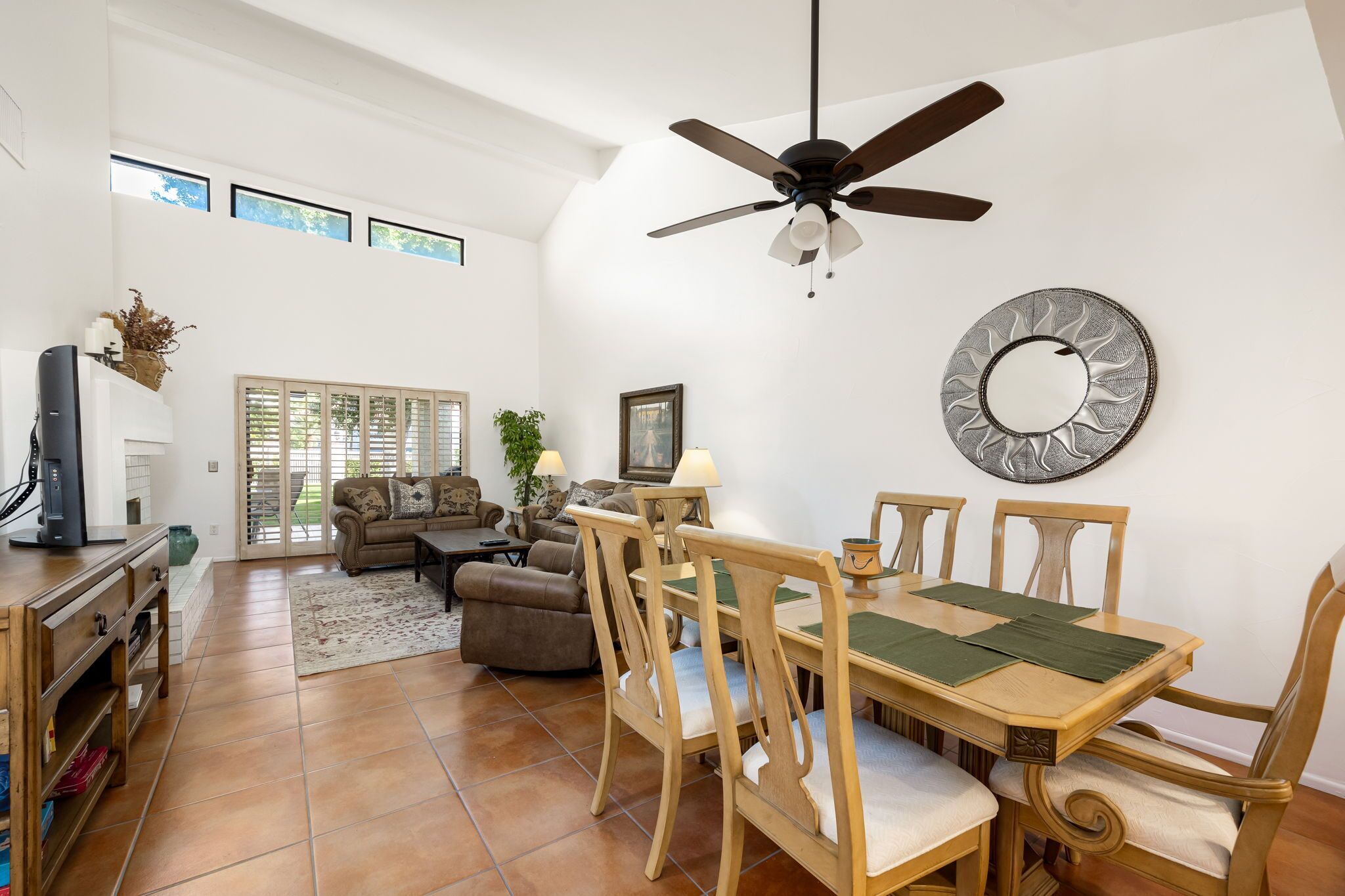A spacious living room with a dining area, a ceiling fan, and a large mirror on the wall.
