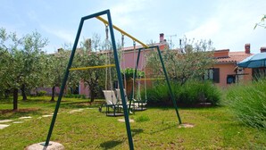 Un parque infantil con columpios y un tobogán, rodeado de césped y árboles.