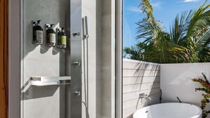 A modern bathroom with a freestanding bathtub, a shower enclosure, and a glass door leading to a balcony with a view of palm trees. - Studio w/ Private Plunge Pool (Long Bay Hills)