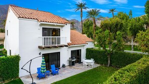 Una casa de dos pisos con techo de tejas, un balcón y un patio con mobiliario exterior.