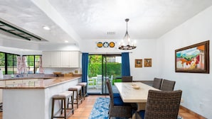 Una cocina amplia con una isla central, taburetes de bar y un comedor con una mesa grande y sillas de mimbre.