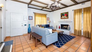 Una sala de estar con chimenea, un sofá, un banco y un tapete estampado.