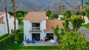 Una casa de dos pisos con techo de tejas, un balcón y un patio con mobiliario exterior.