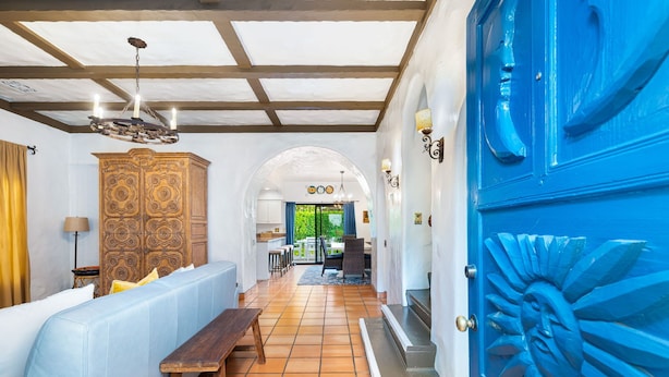 Una habitación amplia con un sofá blanco, un banco de madera y una puerta azul grande con un diseño de sol.