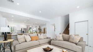 A spacious living area with a large sofa set, a coffee table, and a kitchen in the background. - Tennis Villa #10, Close to Festivals!   Pet Friendly Home.  Permit 063443 (La Quinta)