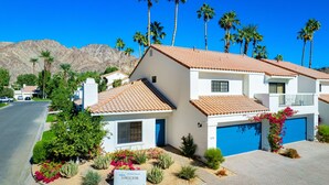 A two-story house with a tiled roof, surrounded by palm trees and a mountain in the background. - Tennis Villa #10, Close to Festivals!   Pet Friendly Home.  Permit 063443 (La Quinta)