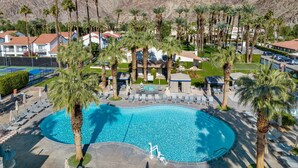 Un resort con una gran piscina rodeada de palmeras y sillones de descanso, con montañas al fondo.
