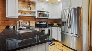 A modern kitchen with white cabinets, stainless steel appliances, and a granite countertop. - Callie's Cabin on the Creek: 3BR w/ Firepit, Dock & Canoe | Pet Friendly (Highlands)