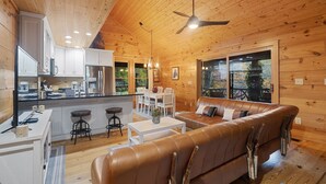A cozy cabin interior with a wooden ceiling, a dining area, a sofa, and a kitchen. - Callie's Cabin on the Creek: 3BR w/ Firepit, Dock & Canoe | Pet Friendly (Highlands)
