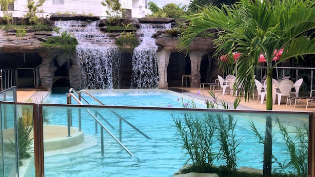 Ein Pool mit Wasserfall, umgeben von Pflanzen und Sitzgelegenheiten im Freien.