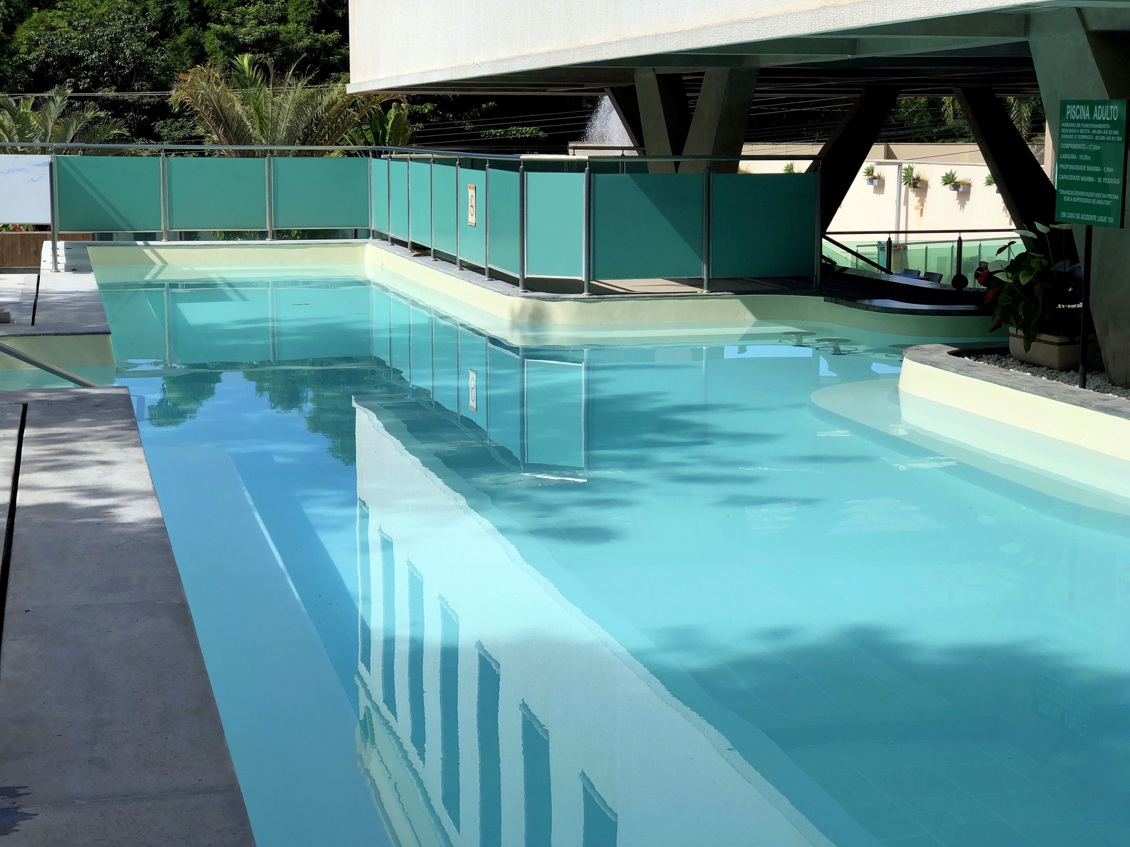 A rectangular swimming pool with a clear blue water surface, surrounded by a green fence and concrete steps leading into the pool.