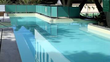 A rectangular swimming pool with a clear blue water surface, surrounded by a green fence and concrete steps leading into the pool.