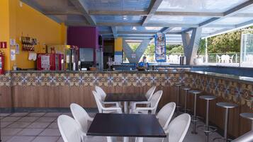 A restaurant with a bar area, white plastic chairs, and a tiled floor.