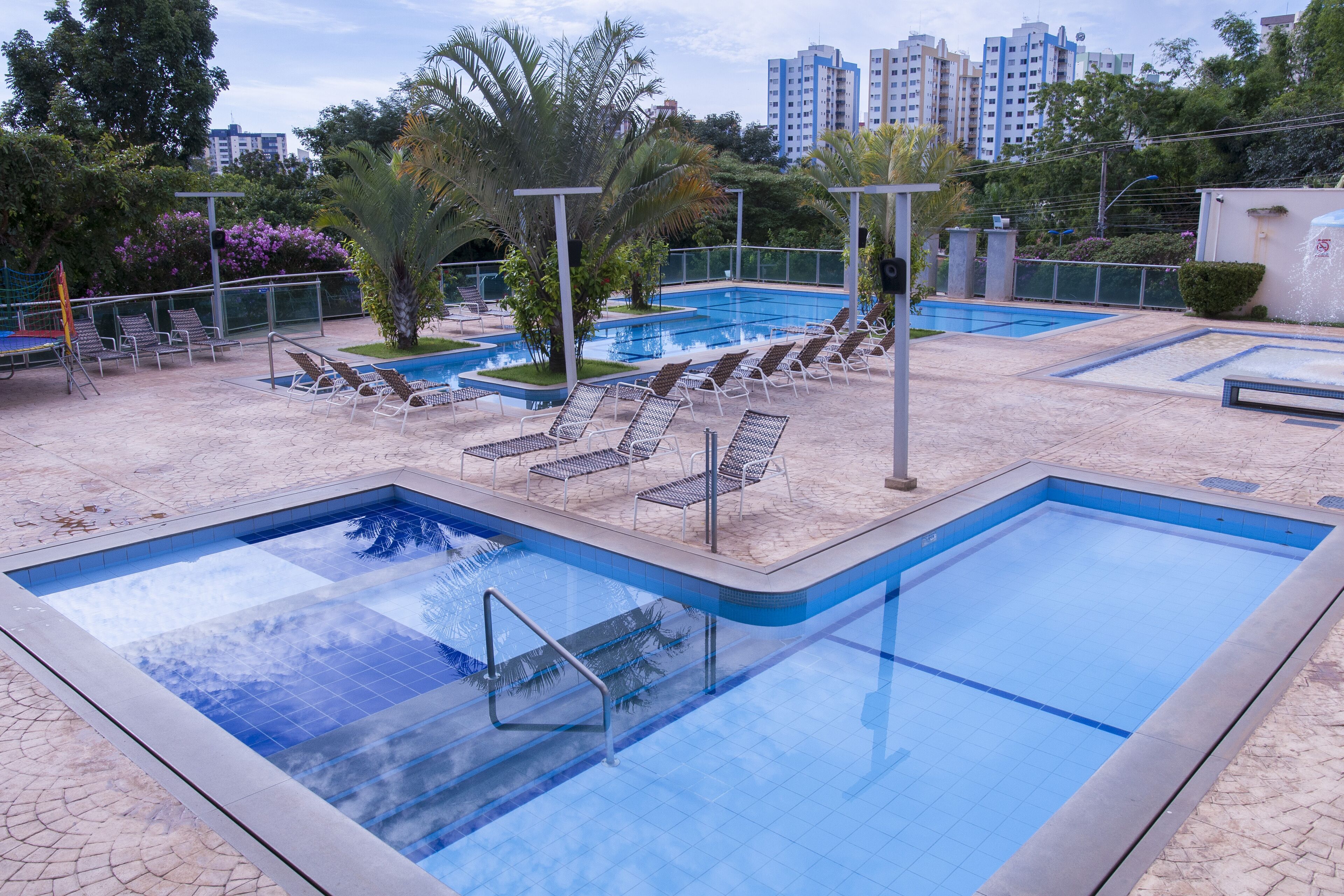 Une piscine dotée de plusieurs couloirs, entourée de chaises longues et de palmiers.