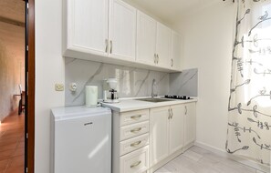 A compact kitchen with white cabinets, a white refrigerator, a marble backsplash, and a window with a bird pattern curtain.