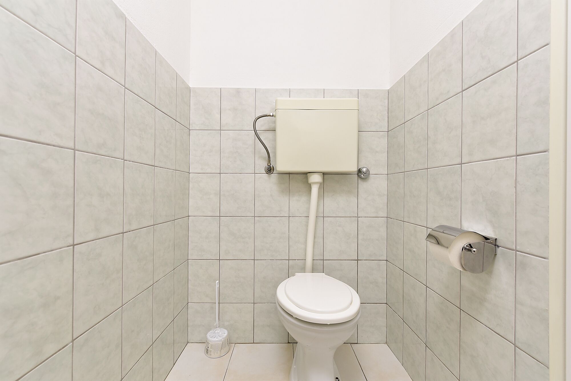 Ein kleines, sauberes Badezimmer mit Toilette, Toilettenpapierhalter und einem Mopp.