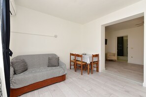 A room with a striped sofa, a dining table with chairs, a shower area, and a door with a sign.