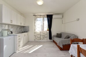 A compact room with a kitchenette, a bed with striped bedding, and a window with a curtain.