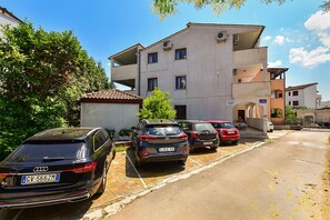 A row of parked cars along a residential street with a multi-story building in the background.