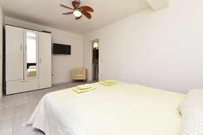 Quarto com cama, uma cadeira, guarda-roupa, televisão e ventoinha no teto.