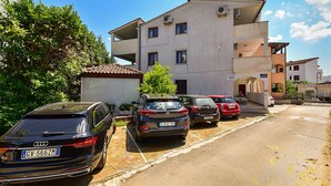 A residential street with parked cars, a two-story building with balconies, and a clear blue sky. - Apartment 85/142 (Istria - Fažana), 50m from the beach (Fažana)