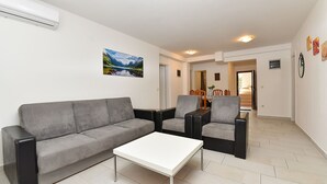 A modern living room with a grey sofa, two armchairs, a white coffee table, and a dining area with a table and chairs. - Apartment 85/142 (Istria - Fažana), 50m from the beach (Fažana)