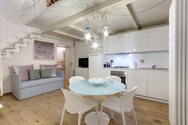 A modern kitchen with white cabinets, a dining table with white chairs, and a staircase leading to another level.