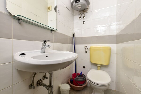 Un baño con un lavabo blanco, grifo cromado y un inodoro amarillo.