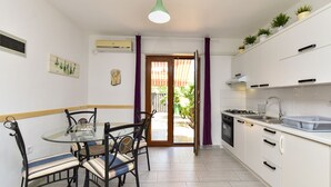 Una cocina compacta con comedor, una mesa pequeña, sillas, una lámpara colgante y vistas a un área exterior por una puerta.