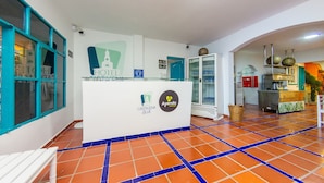 A hotel reception area with a tiled floor, a reception desk, and a kitchen in the background.