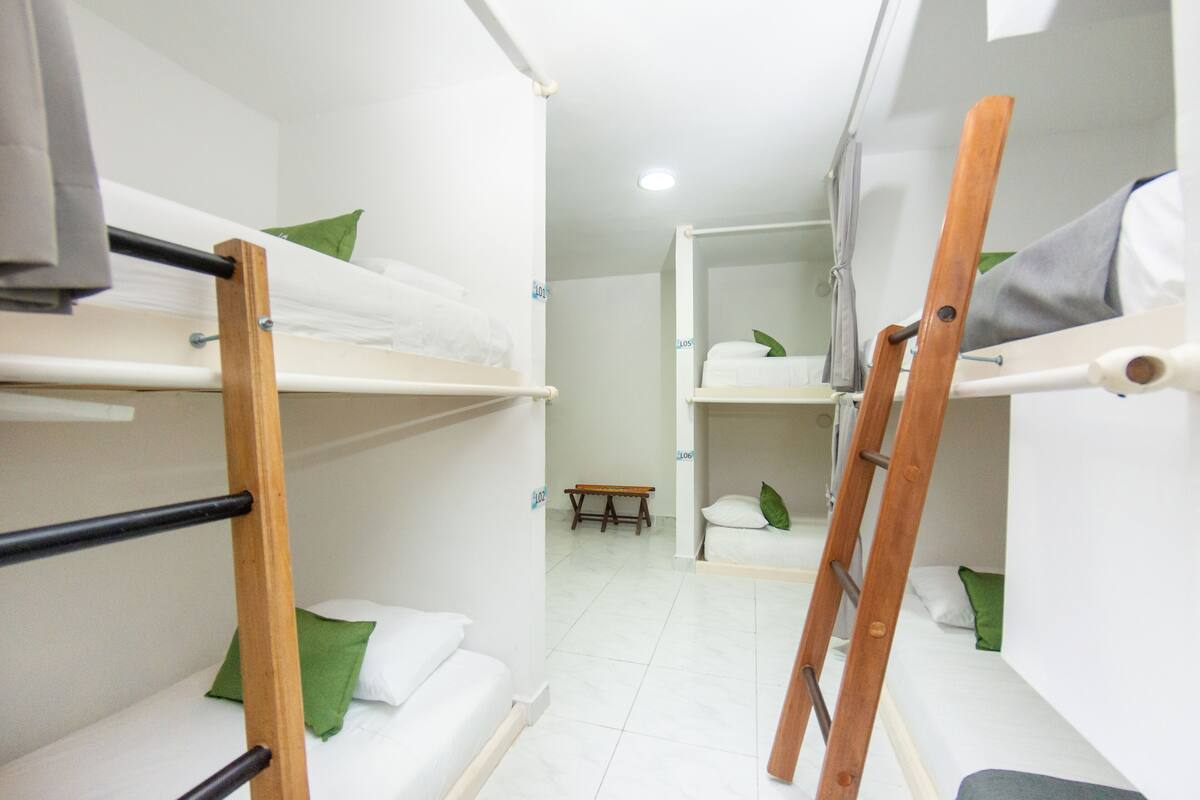 A dormitory room with bunk beds, a wooden ladder, and a small bench.