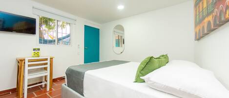 A bedroom with a bed, a small table, a TV, a window, and a door.