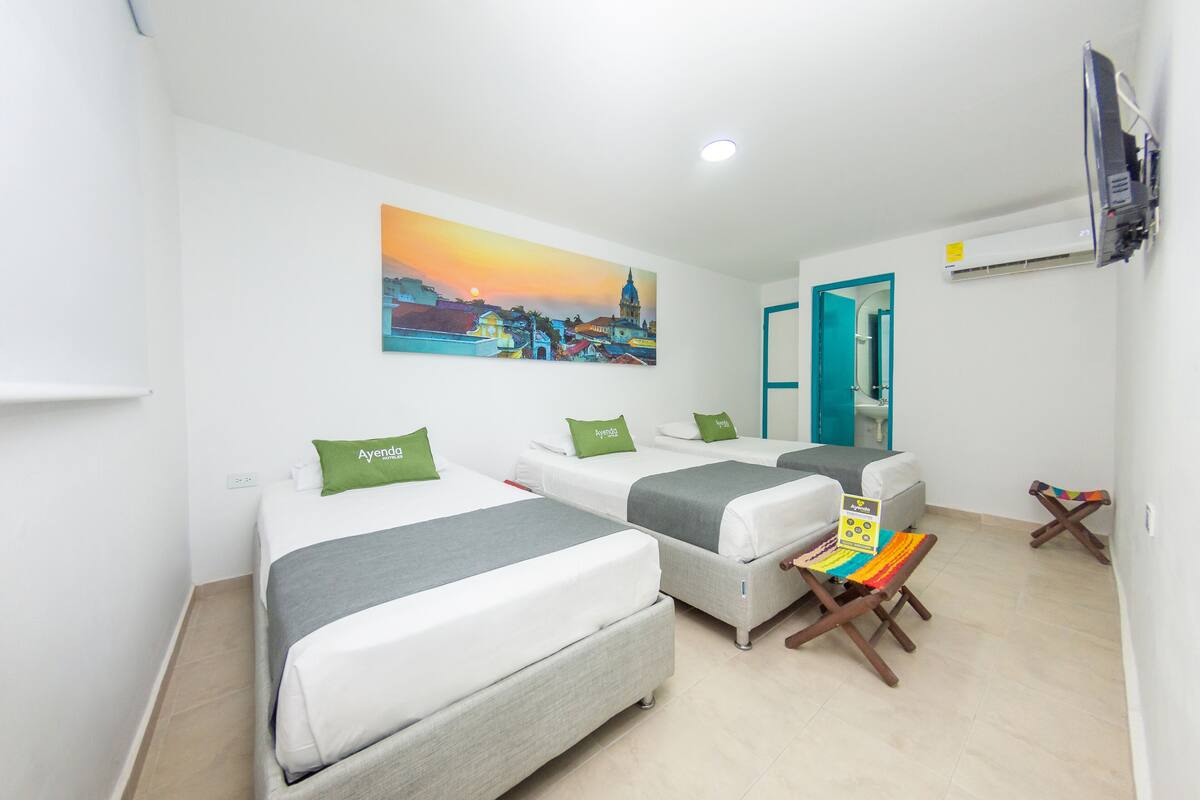 A hotel room with two beds, a painting of a cityscape, a TV mounted on the wall, and a small table with a chair.