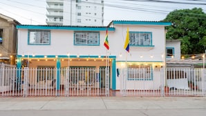 A building with a white facade and blue trim, featuring a gated entrance with string lights.