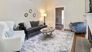A living room with a white armchair, a dark sofa, a coffee table, and a blue armchair. There is a fireplace, a lamp, and a mirror on the wall. - Heated Pool Access | 5*Clean | Flex Cancelation (Savannah)