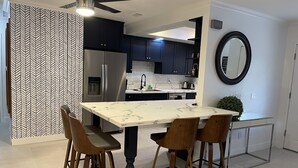 Une cuisine moderne avec des meubles de couleur sombre, un réfrigérateur en acier inoxydable et un îlot en marbre agrémenté de tabourets de bar.