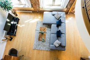 Un salon moderne avec un canapé d’angle gris, une table basse en bois et un téléviseur posé sur un meuble.