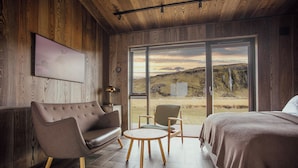 A modern room with a wooden interior, a large window with a view of a landscape, a sofa, a chair, and a bed. - Seljalandsfoss Horizons (Rangárþing eystra)