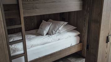 Una cama litera con ropa blanca y almohadas, estructura de madera y una escalera.