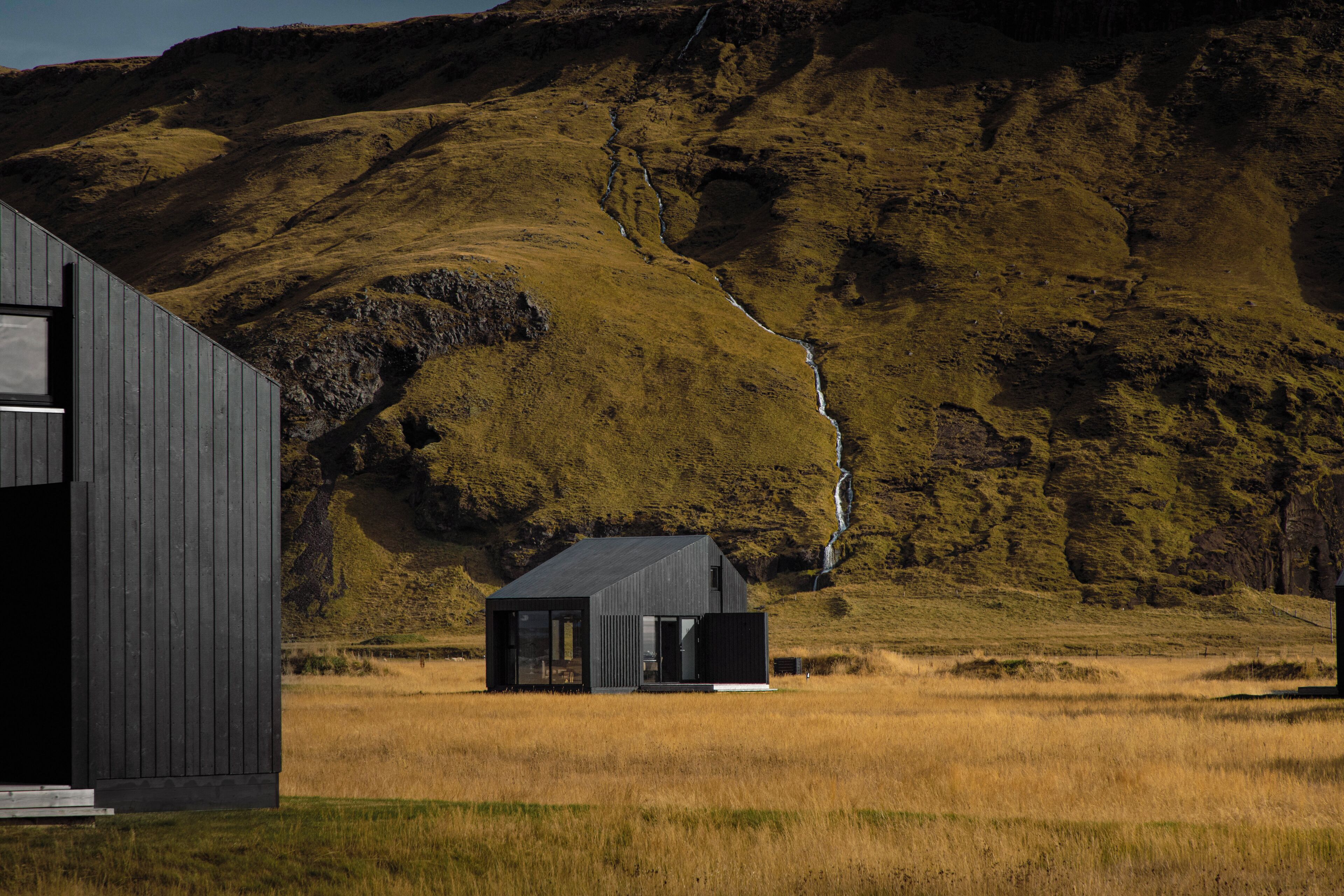 A modern building with a large window and a door, set in a grassy field with a mountain in the background.