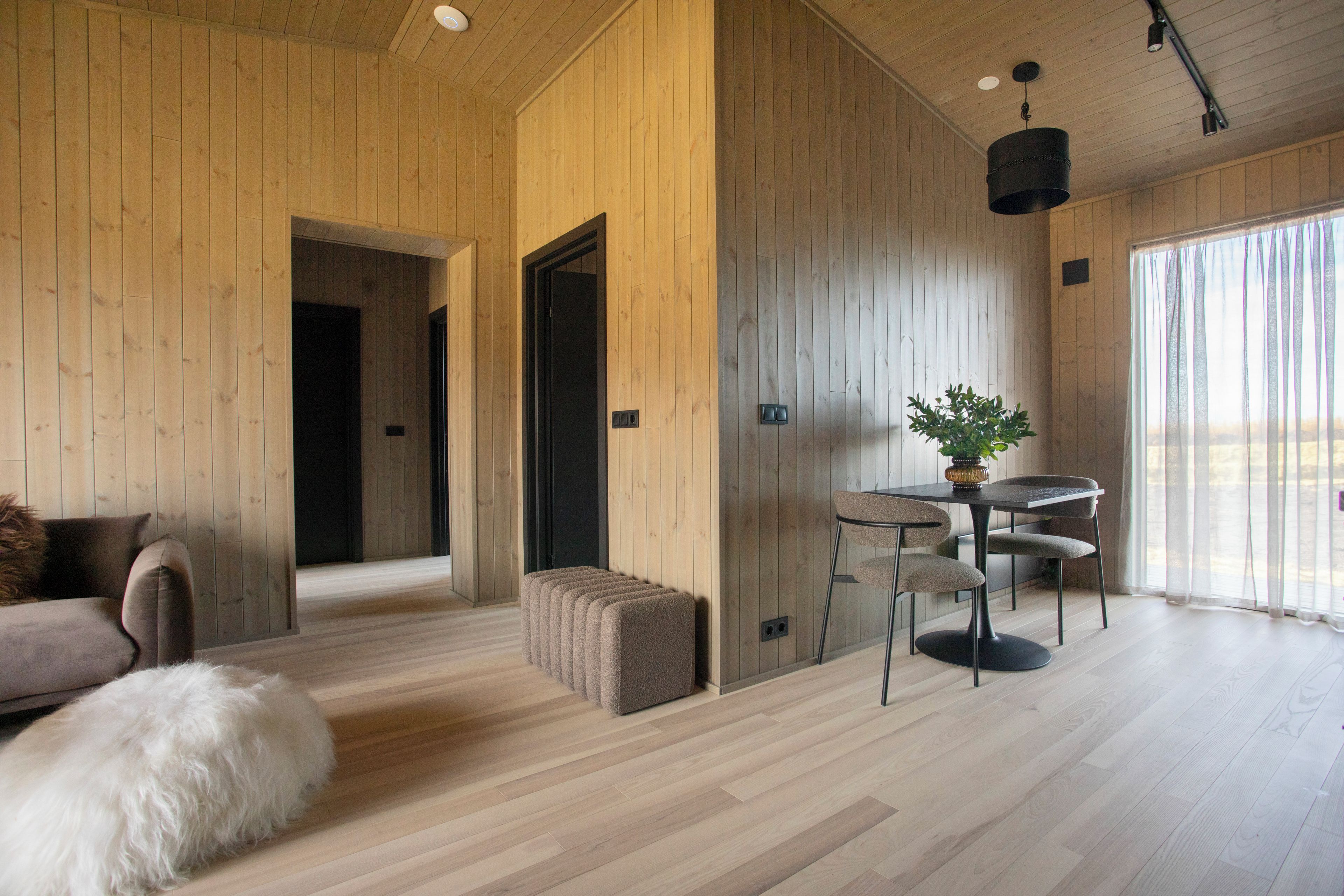 A modern interior with wooden walls, a dining area with a table and chairs, a sofa, and a fluffy white dog.