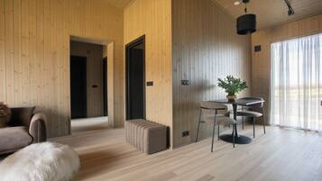 A modern interior with wooden walls, a dining area with a table and chairs, a sofa, and a fluffy white dog.
